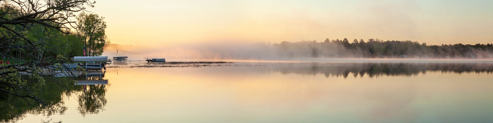 Panorama of a calm northern Minnesota lake and fog at dawn during spring with docks along the shoreline