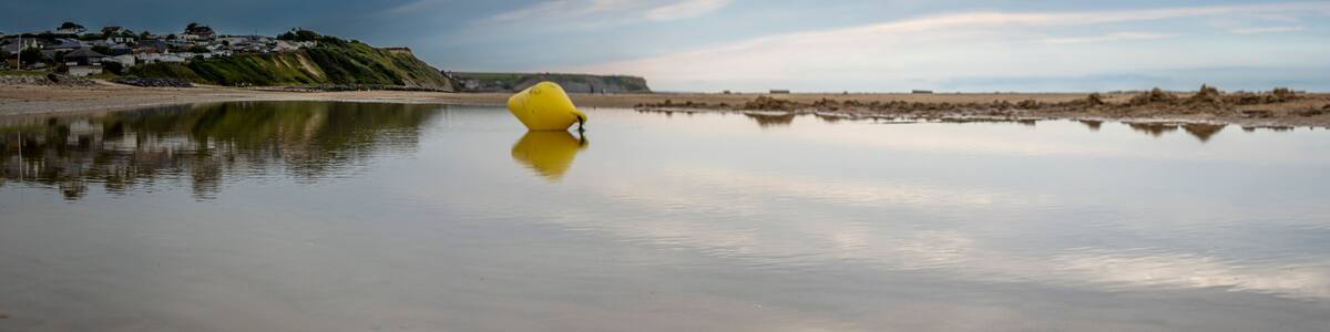Saint-Come-de-Fresne, France - 08 08 2025: Panoramic view of a yellow buoy reflecting on the water, the sea, the beach, the cliff and the city with cloudy sky
