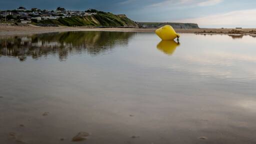 Saint-Come-de-Fresne, France - 08 08 2025: Panoramic view of a yellow buoy reflecting on the water, the sea, the beach, the cliff and the city with cloudy sky
