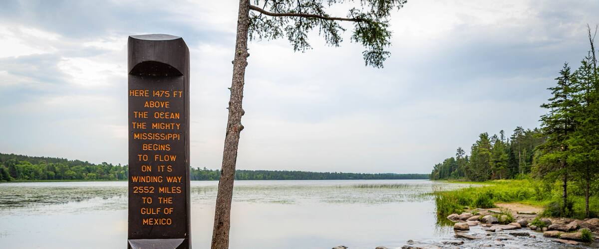 A wooden post with text, a river, and a forested landscape.