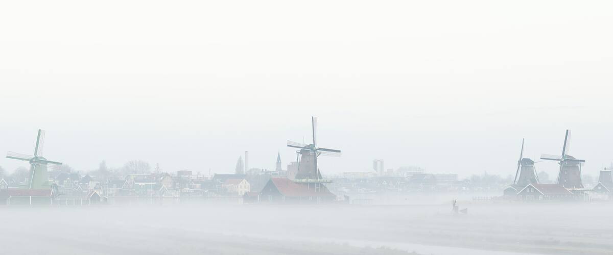 Windmills and houses by a foggy water body.