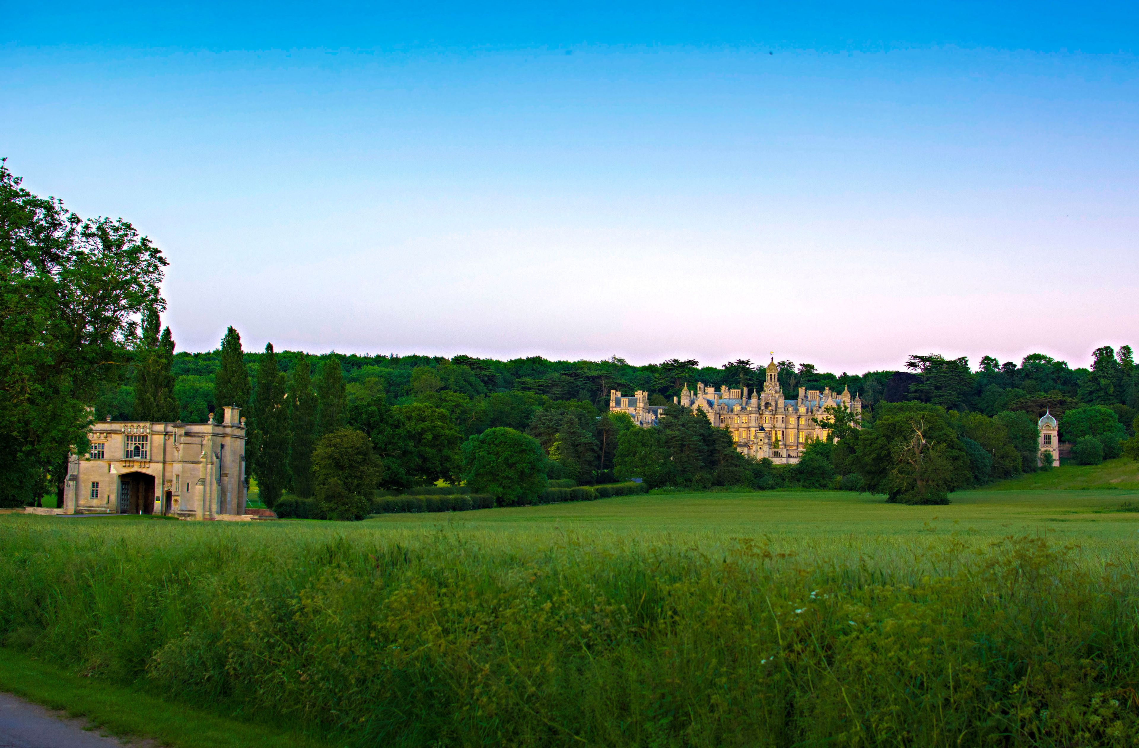 A large, historic building with intricate architecture, surrounded by lush greenery and a field.