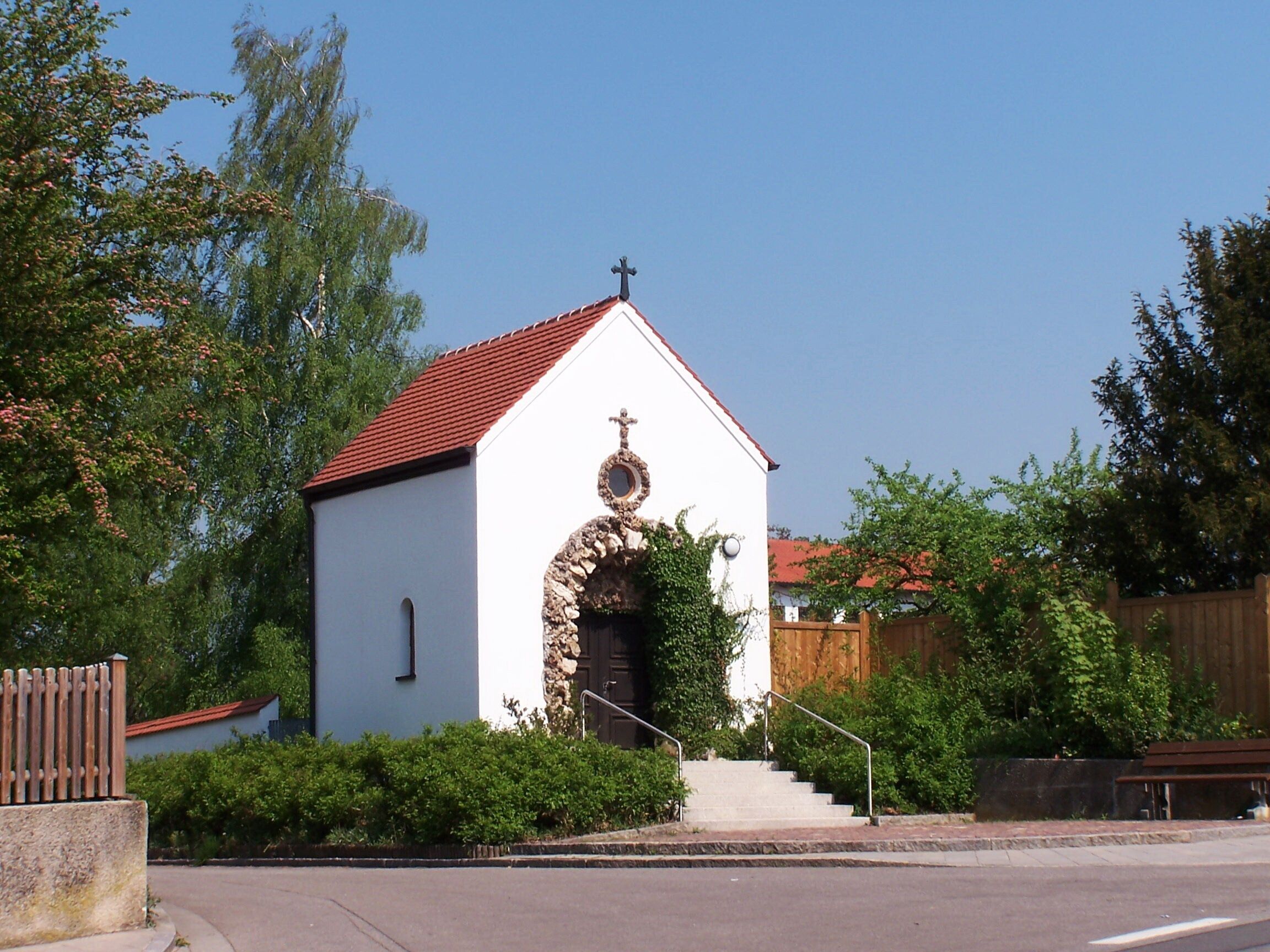 A small white church with a red roof and a stone archway.