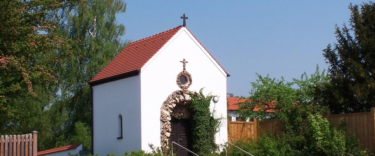 A small white church with a red roof and a stone archway.