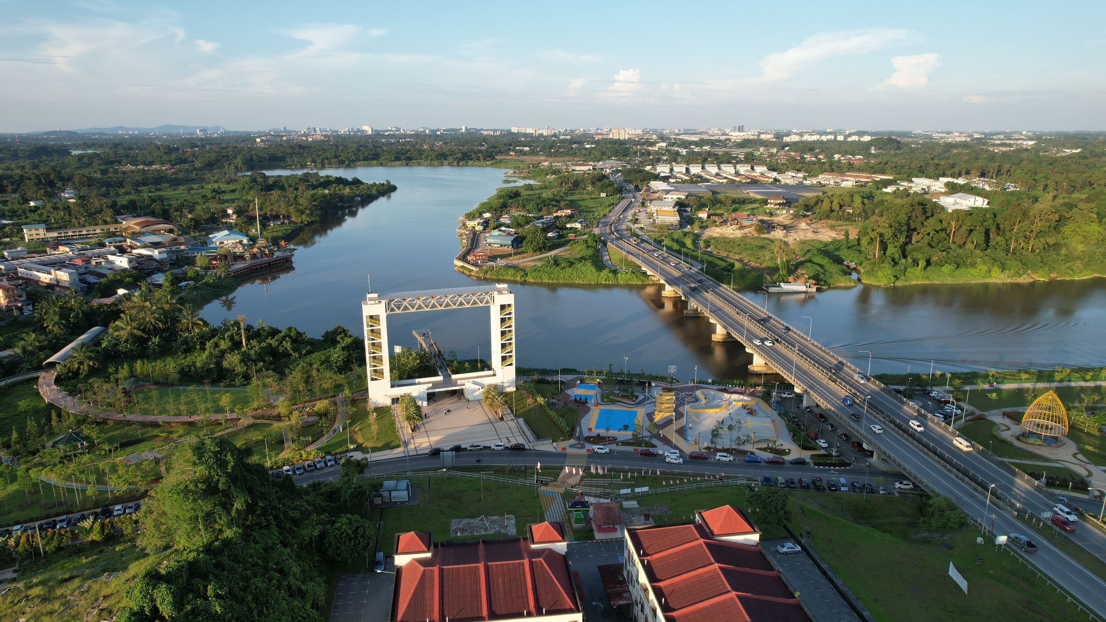 An aerial view of a city with a prominent bridge, a river, and surrounding greenery.