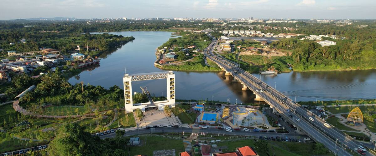 An aerial view of a city with a prominent bridge, a river, and surrounding greenery.