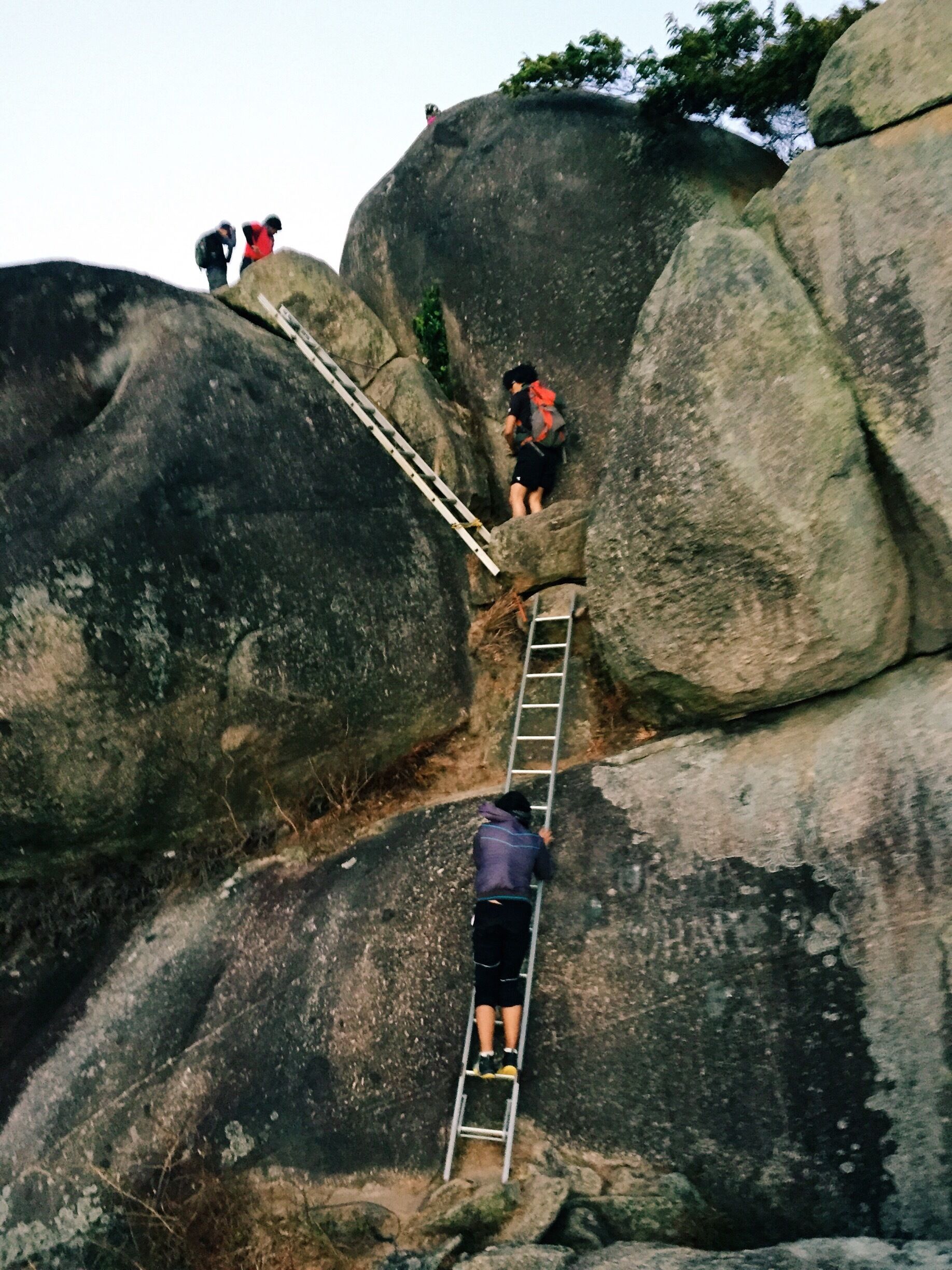 A person climbing a rocky mountain with a ladder.