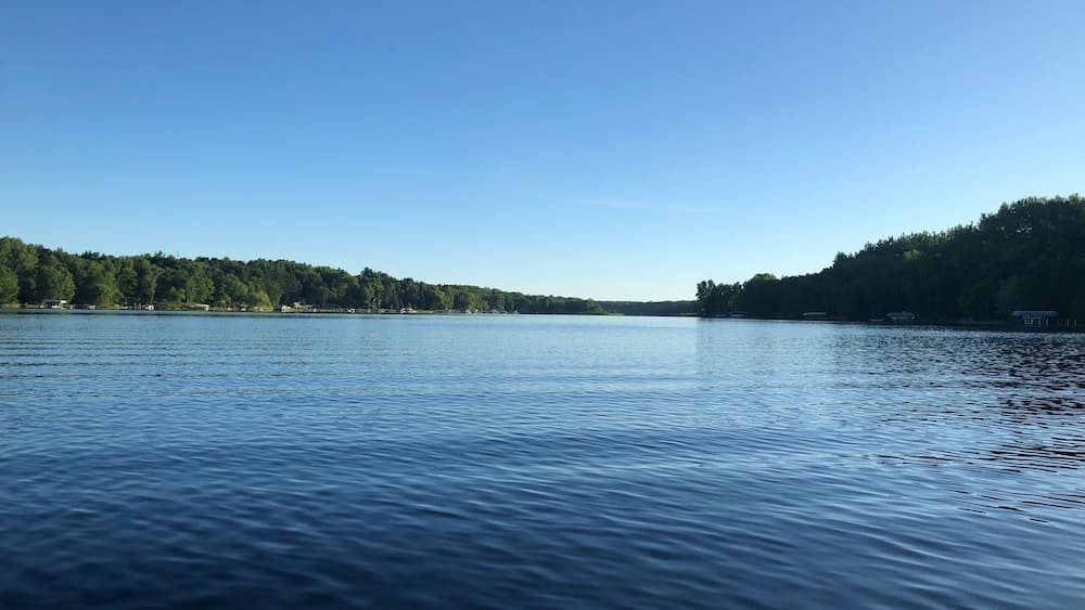 A calm lake with a forested shoreline and a clear sky.