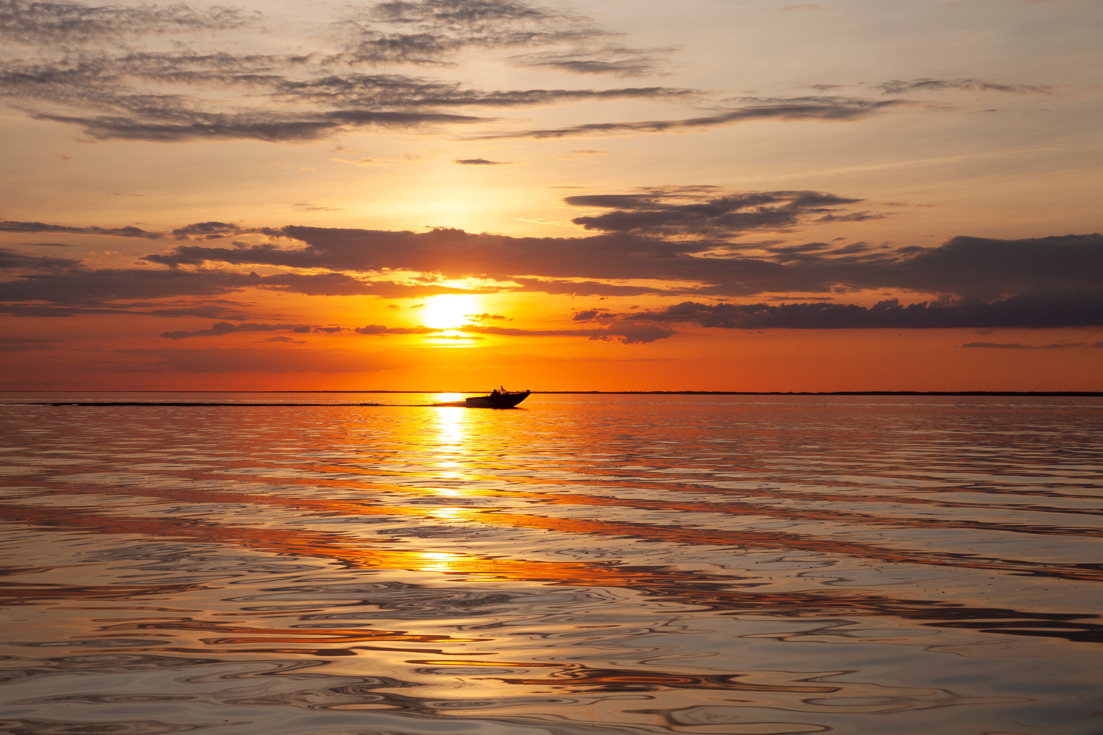 A sunset over a calm sea with a boat in the distance.