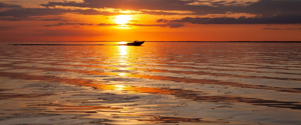 A sunset over a calm sea with a boat in the distance.
