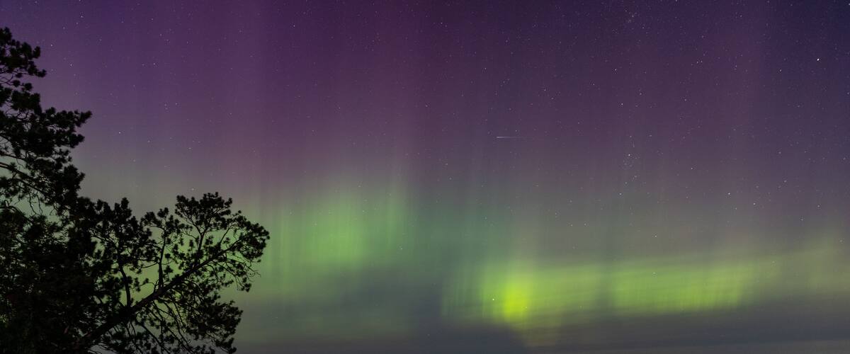 A night sky with the Northern Lights over a calm lake with a dock and trees.