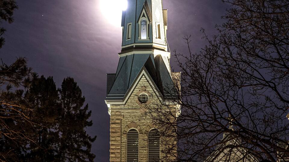 A church steeple with a cross at the top, under a full moon.