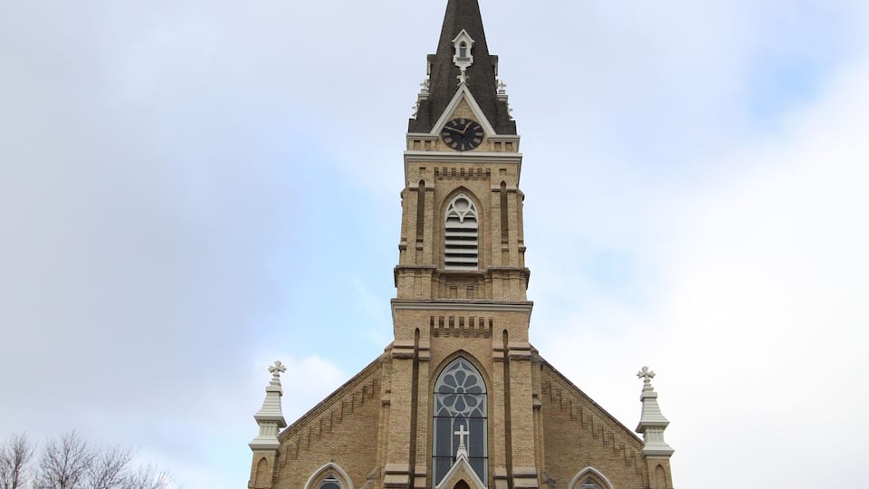A church with a tall steeple, arched windows, and a cross at the top.