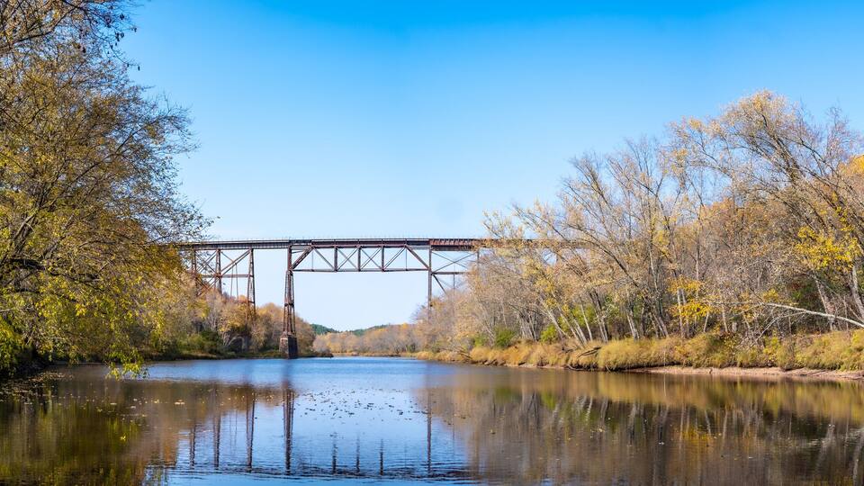 A river with a bridge, surrounded by autumn-colored trees.
