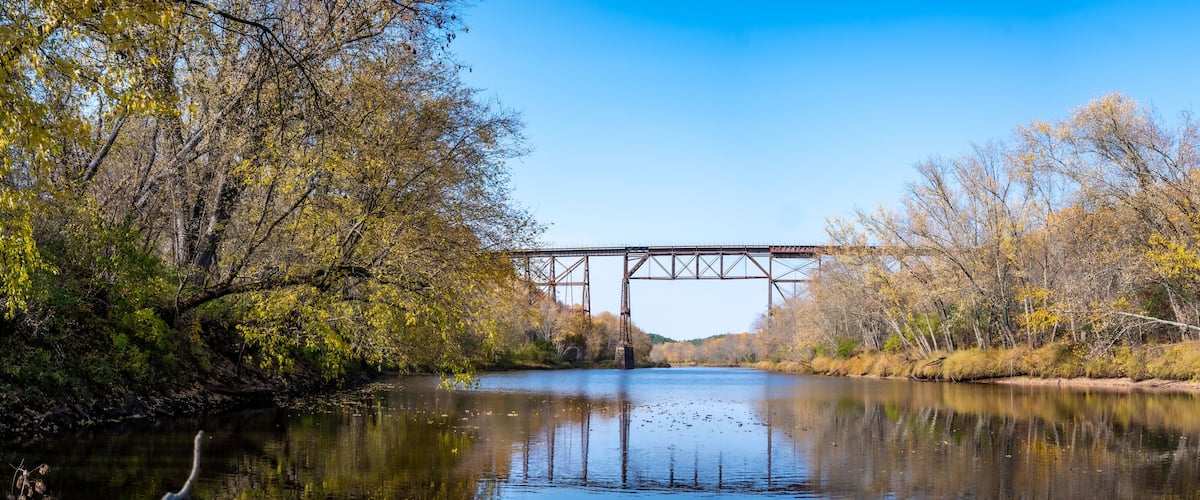 A river with a bridge, surrounded by autumn-colored trees.