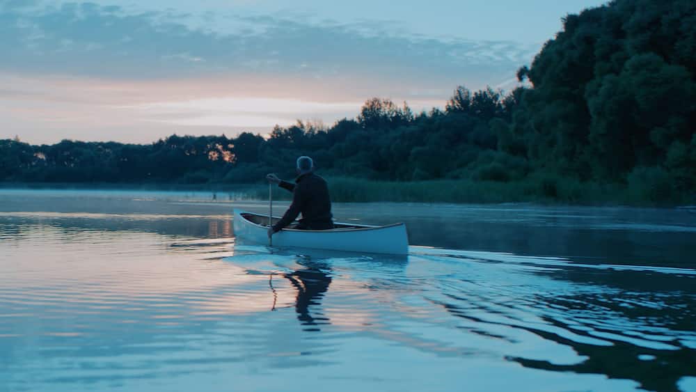 Man canoeing in a traditional wooden boat on a large lake at dawn