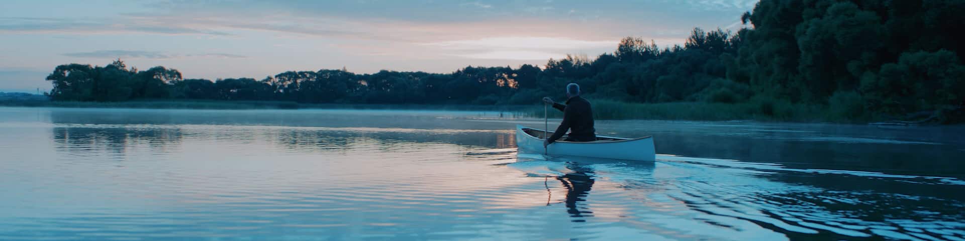Man canoeing in a traditional wooden boat on a large lake at dawn