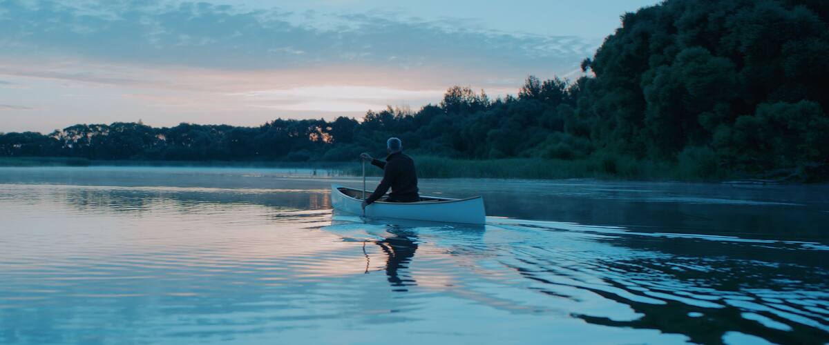 A person in a canoe on a calm lake with trees in the background.
