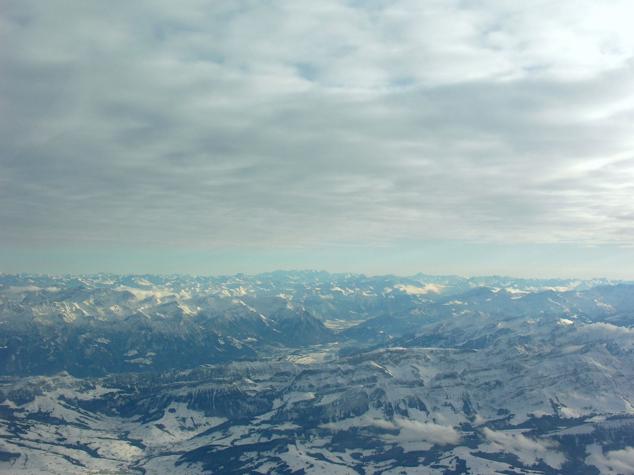 A snow-covered mountain range with a valley and a cloudy sky.