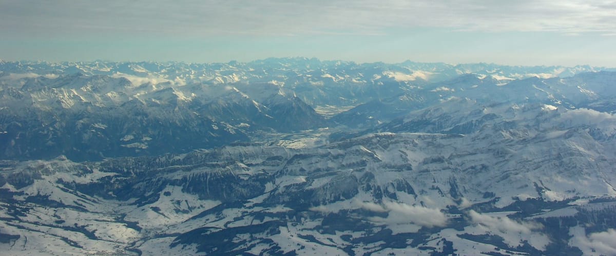 A snow-covered mountain range with a valley and a cloudy sky.