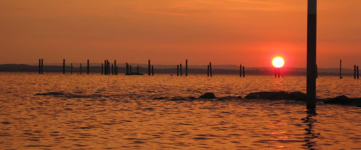 A sunset over a calm body of water with wooden posts in the foreground.