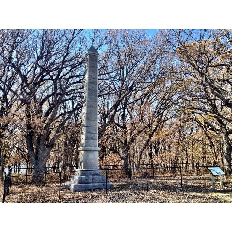A tall stone monument surrounded by leafless trees in a park.