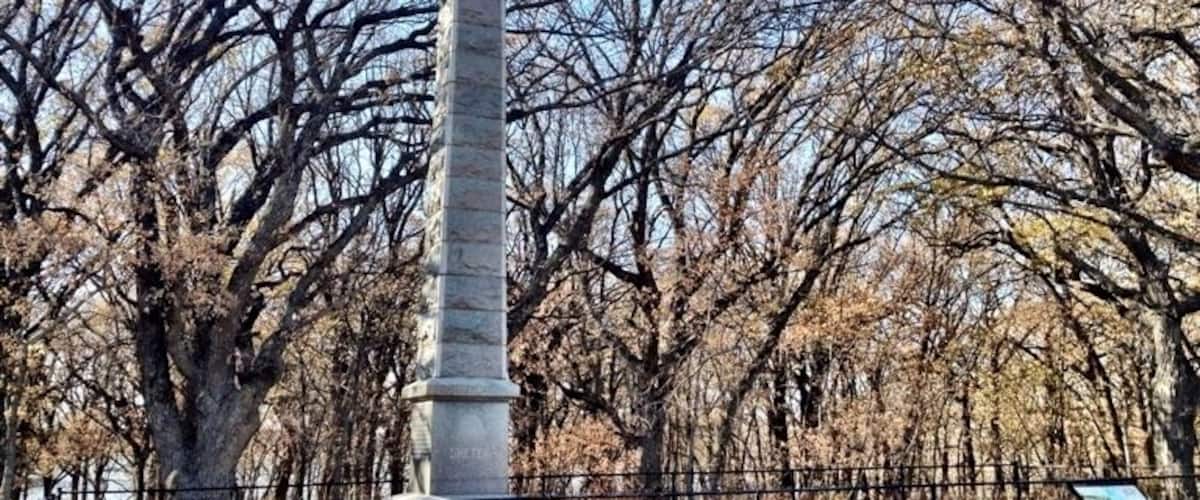 A tall stone monument surrounded by leafless trees in a park.
