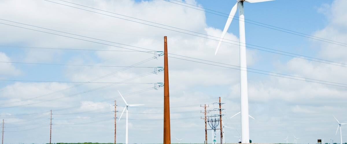 Wind turbines, power lines, and a grassy field under a blue sky.