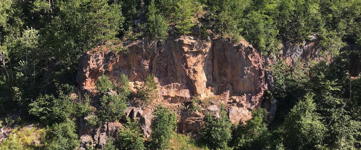 A rocky cliff surrounded by dense green forest.