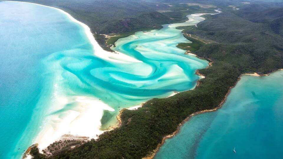 An aerial view of a coastal area with turquoise waters, white sandy beaches, and dense green forests.