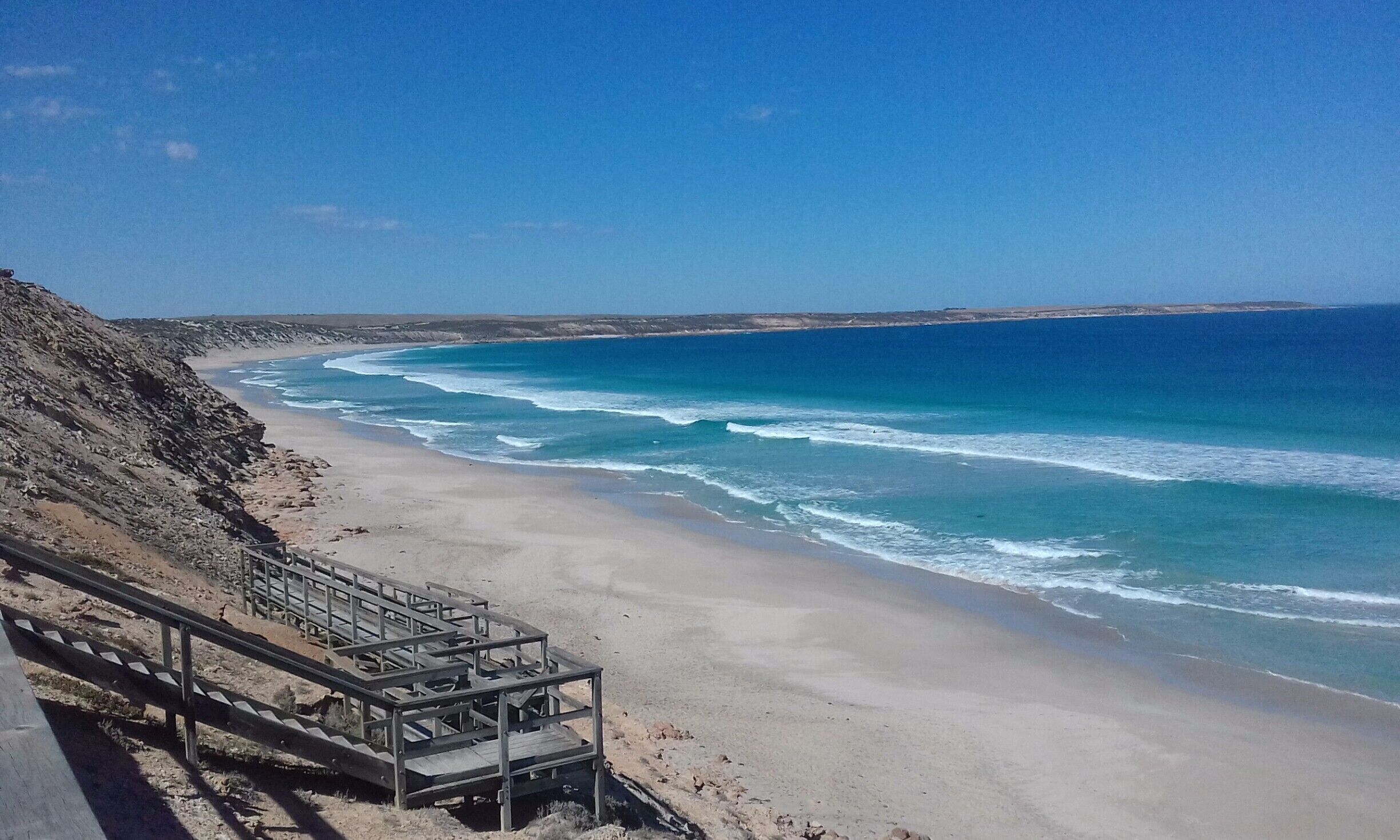 A coastal beach with a wooden staircase leading down to the shore.
