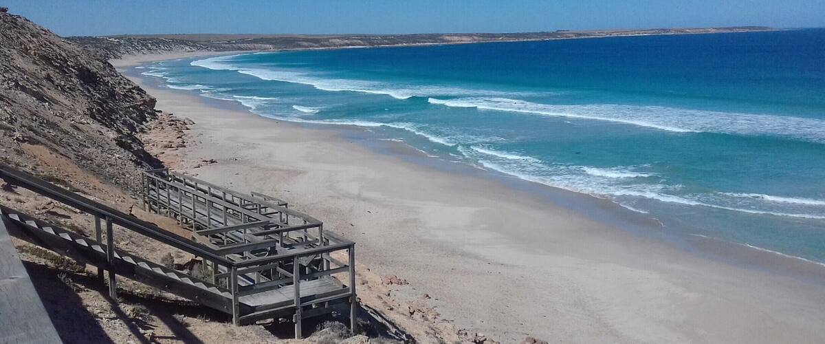 A coastal beach with a wooden staircase leading down to the shore.