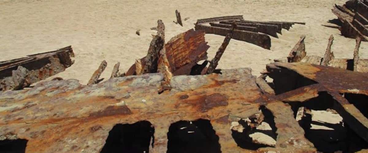 A beach with rusted shipwrecks and a clear blue ocean.