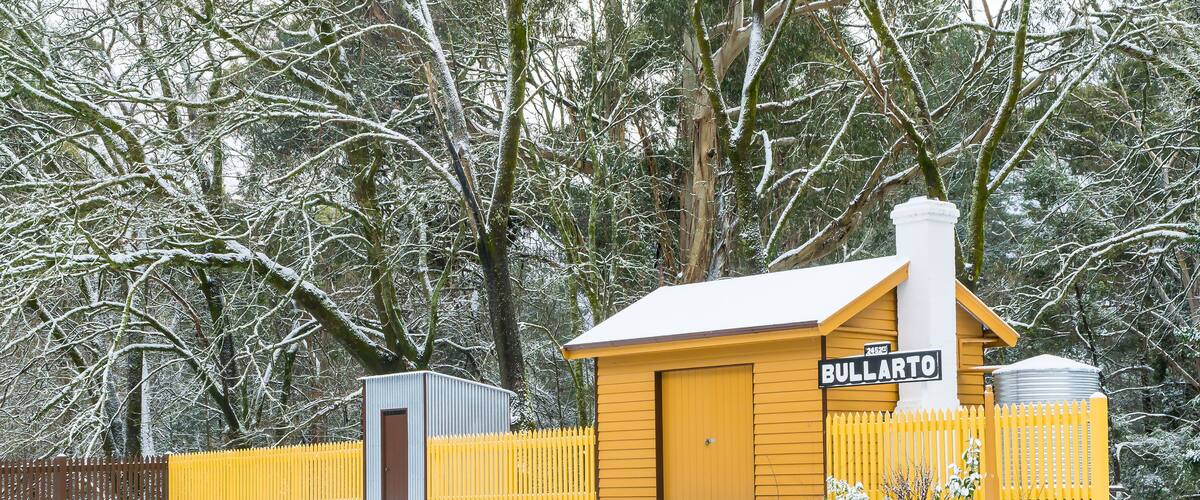A snow-covered railway station named Bullarto with a yellow fence and a brick wall.