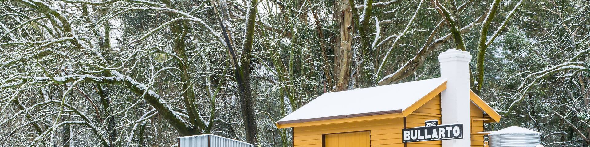 A small yellow railway station on a platform covered in snow