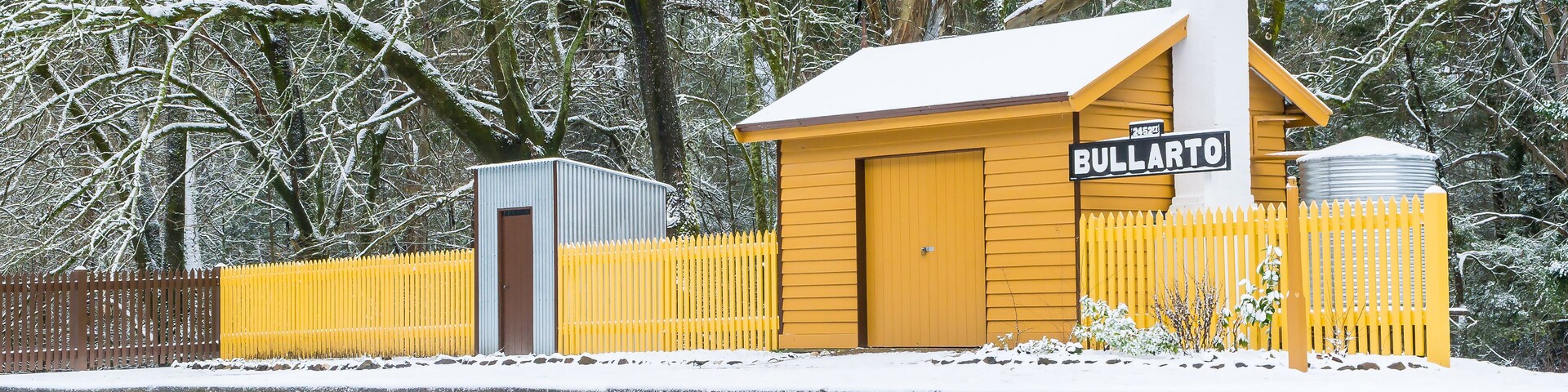 A snow-covered railway station named Bullarto with a yellow fence and a brick wall.