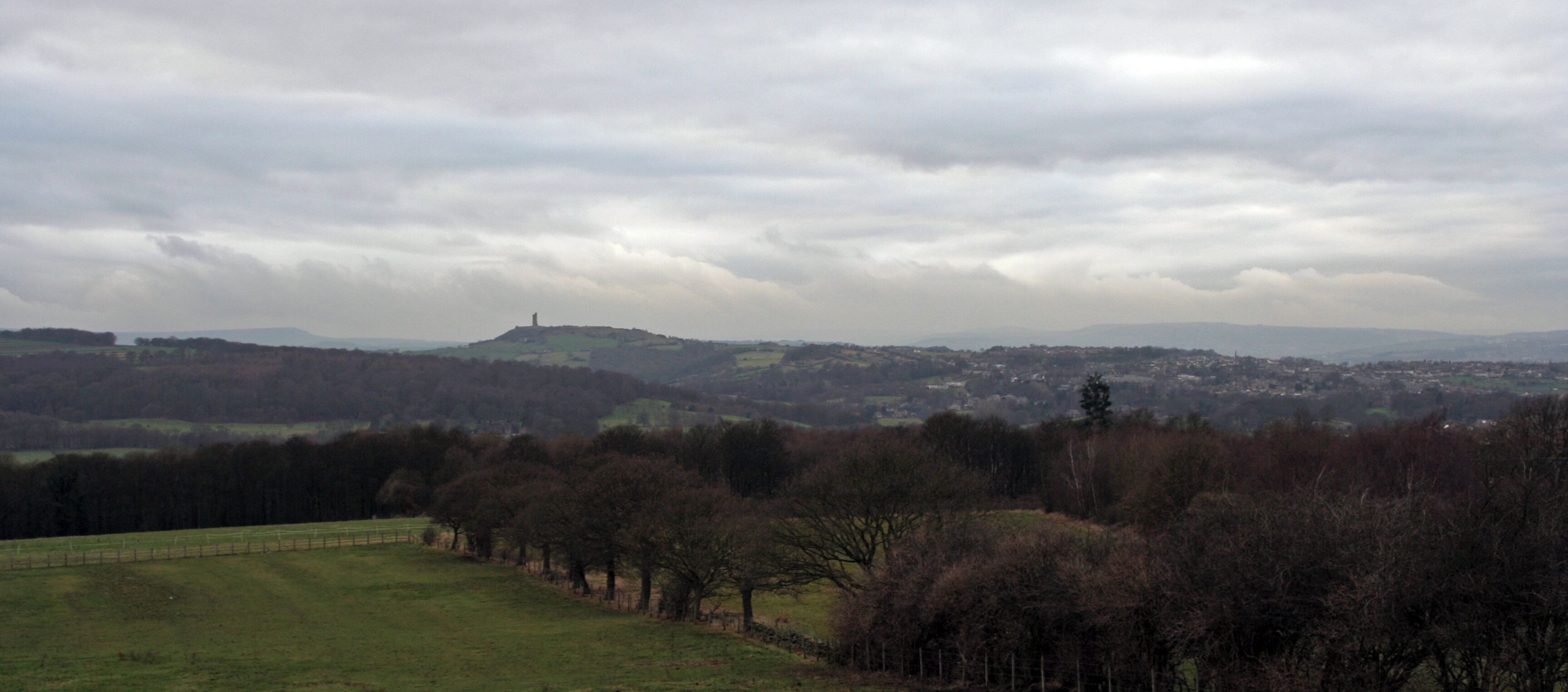 A rural landscape with rolling hills, a distant hilltop structure, and a town in the background.