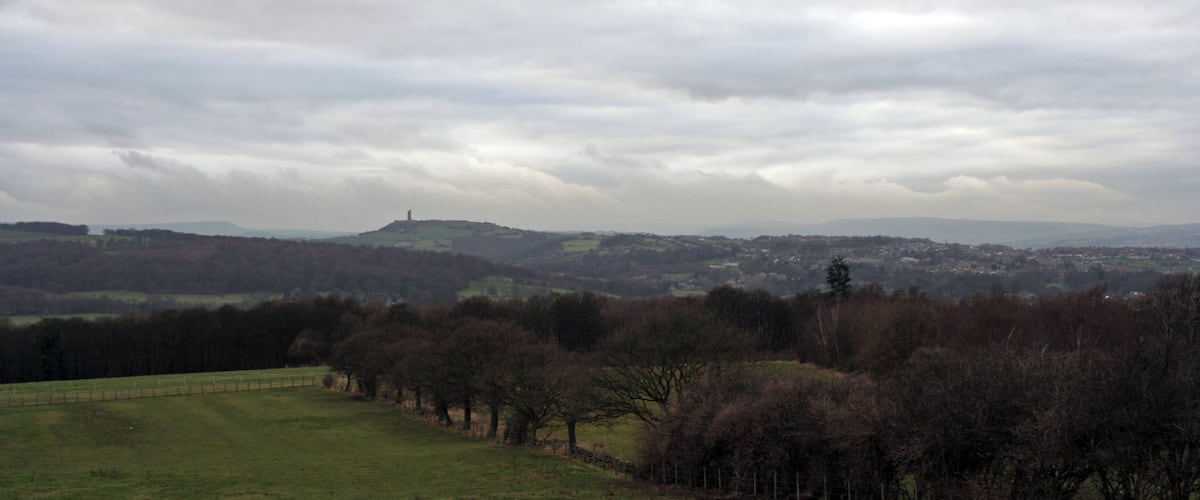 A rural landscape with rolling hills, a distant hilltop structure, and a town in the background.