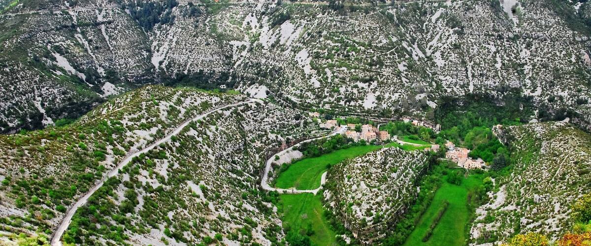 A mountainous landscape with a winding road, green fields, and scattered buildings.