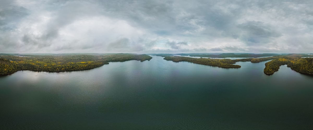 A calm lake surrounded by forested islands under a cloudy sky.