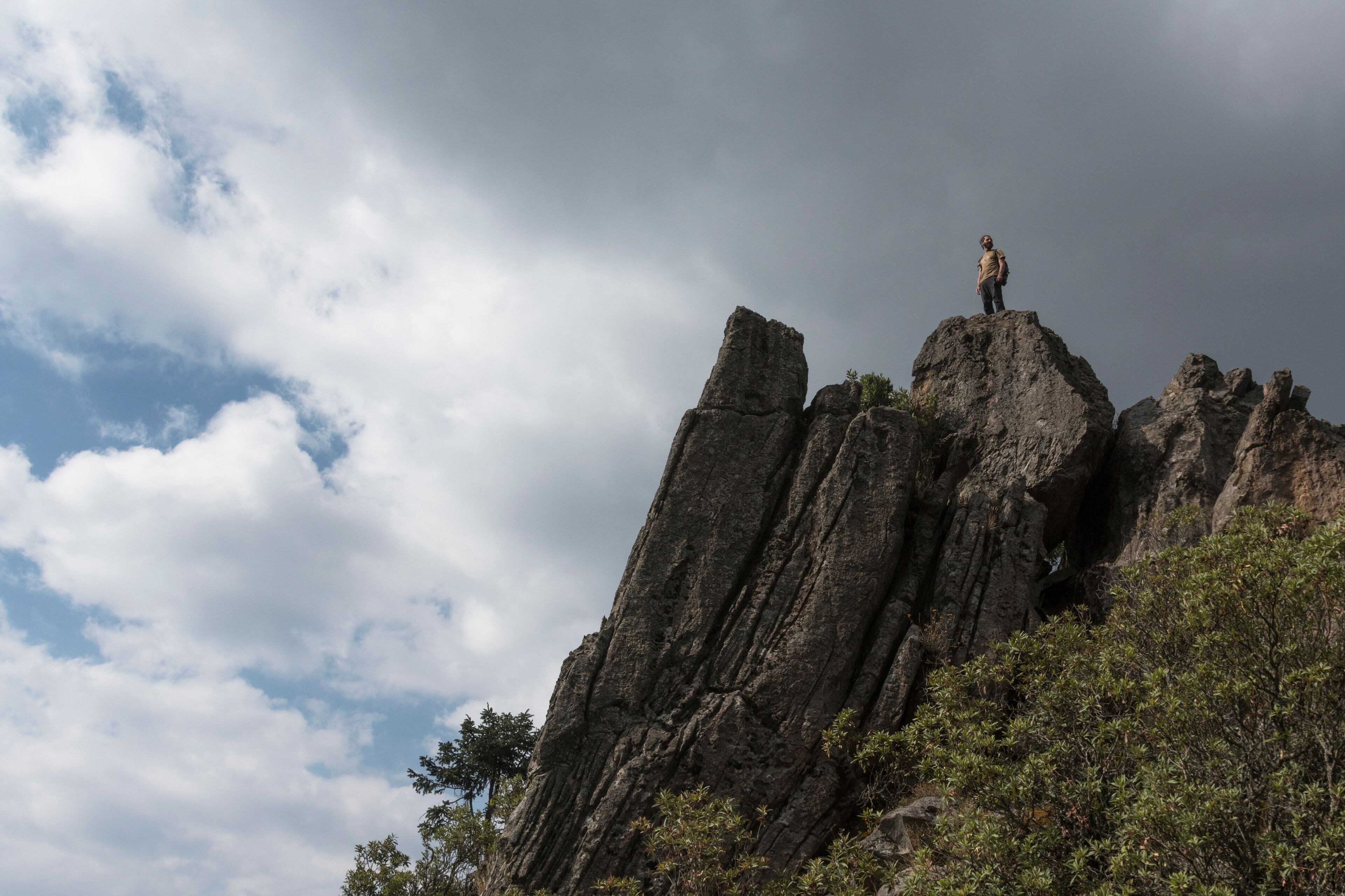 A person standing on a rocky outcrop with a cloudy sky in the background.