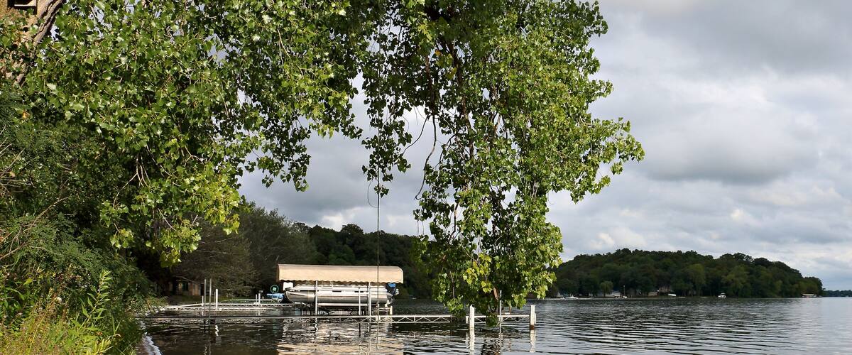 A flooded dock with a covered boat, surrounded by dense greenery and trees.