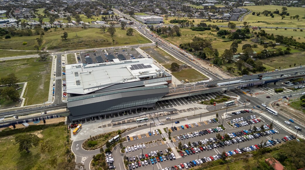 Vue aérienne d’un bâtiment moderne doté d’un grand parking et surplombé par un pont autoroutier.