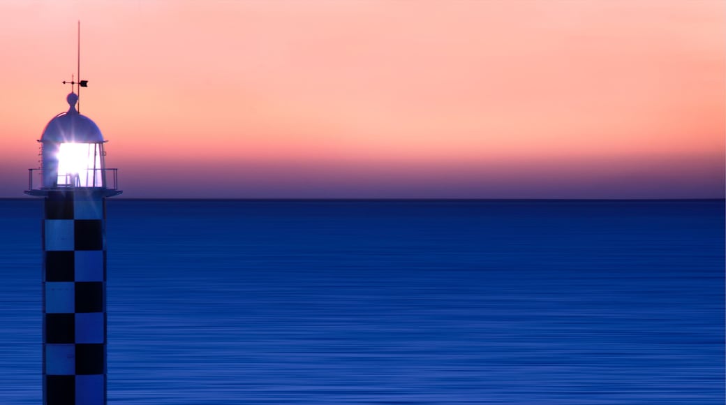 A lighthouse at sunset with a clear sky and calm sea.
