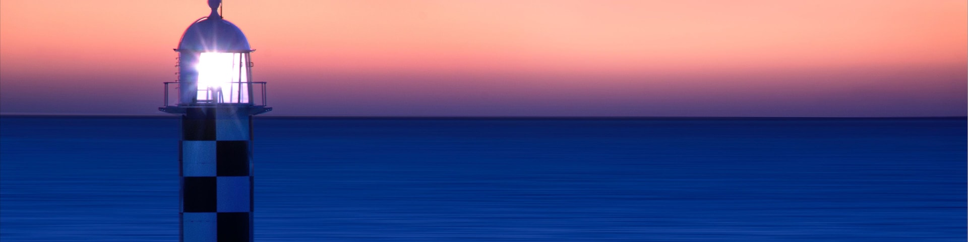 Ein Leuchtturm bei Sonnenuntergang, bewölkter Himmel und ruhige See.
