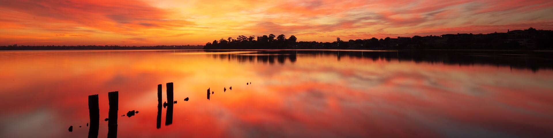 A sunset over a calm lake with a silhouette of trees and a distant shoreline.