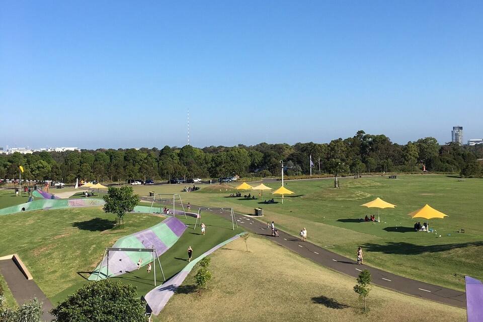 A park with a playground, walking paths, and yellow umbrellas.