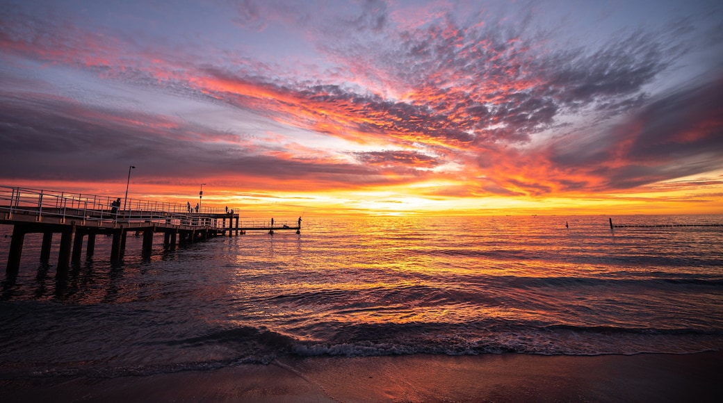 A sunset over a beach with a pier extending into the water.