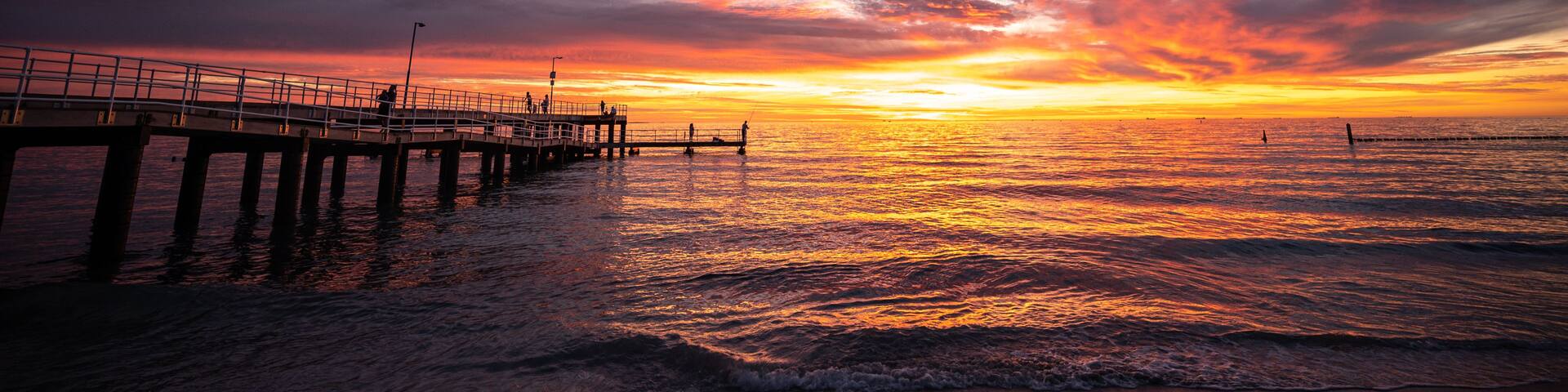 A sunset over a beach with a pier extending into the water.