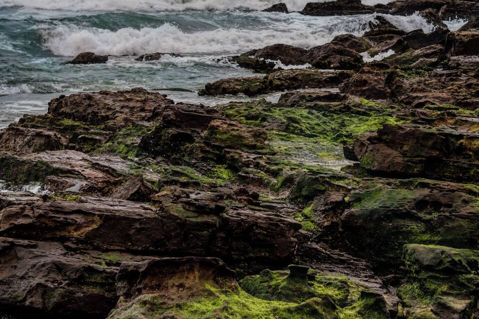A rocky shoreline with waves crashing against the rocks under a cloudy sky.